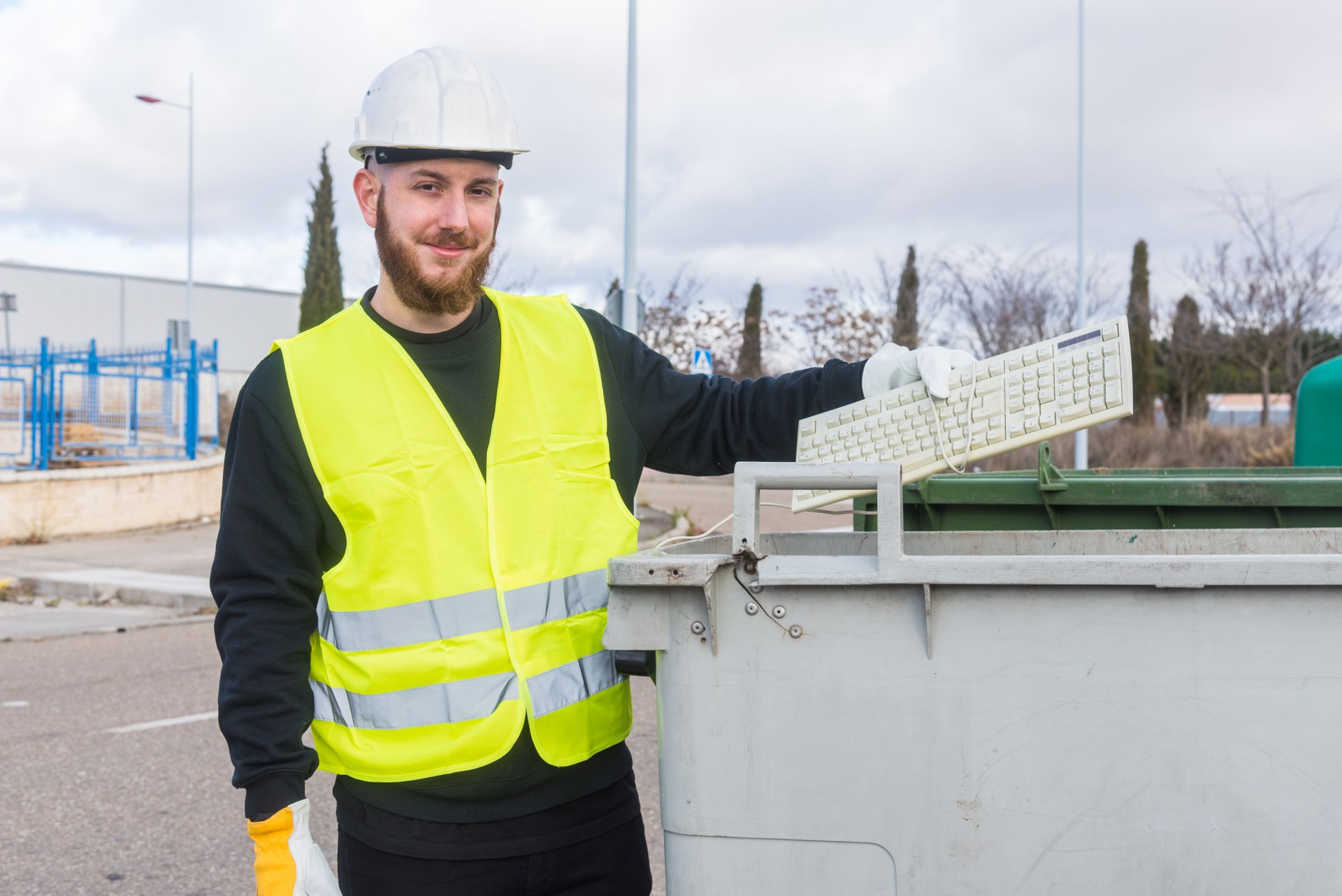 Recycling plant worker throwing an old computer keyboard to a dumpster.